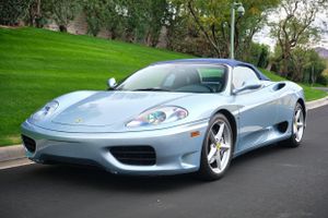 Light blue Ferrari 360 Modena supercar parked on a tree-lined street.