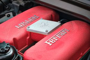 Close-up of red Ferrari engine cover with Ferrari badges and manifold details.