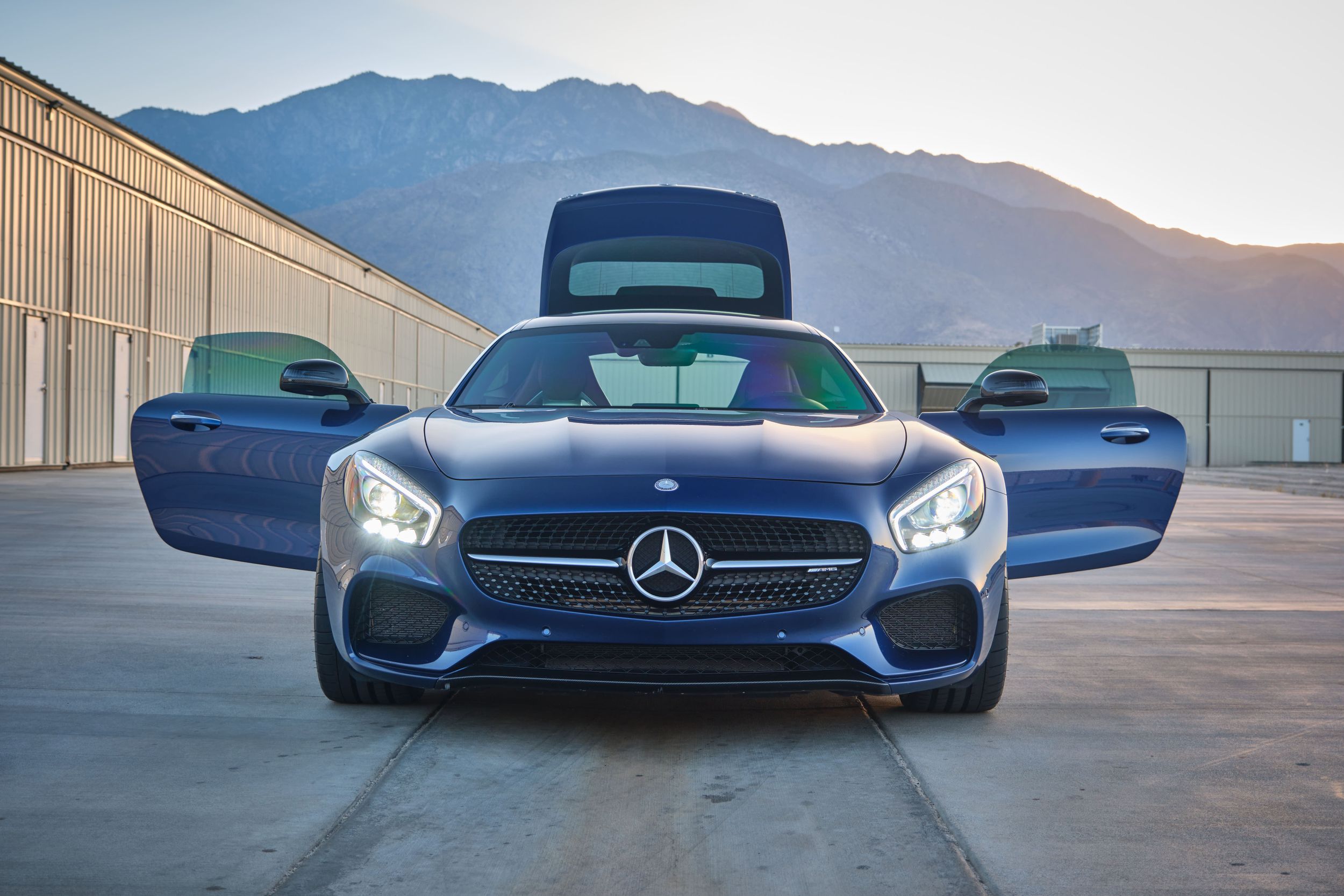 Mercedes AMG GT with doors open showcasing sleek design against mountain backdrop.