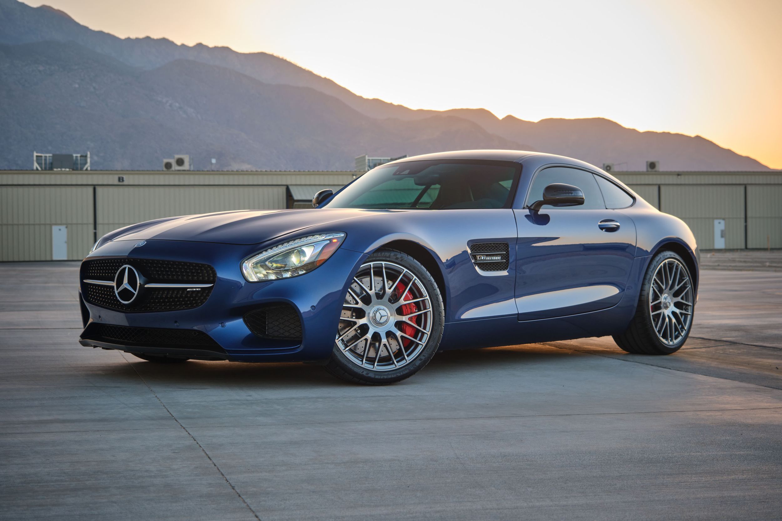 Blue Mercedes AMG GT sports car photographed at sunset with mountains in background.