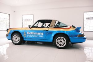 Classic Rothmans-liveried Porsche 911 race car in blue and white displayed in a gallery setting.
