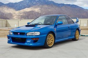 Blue Subaru WRX STI with gold wheels parked in front of mountains.
