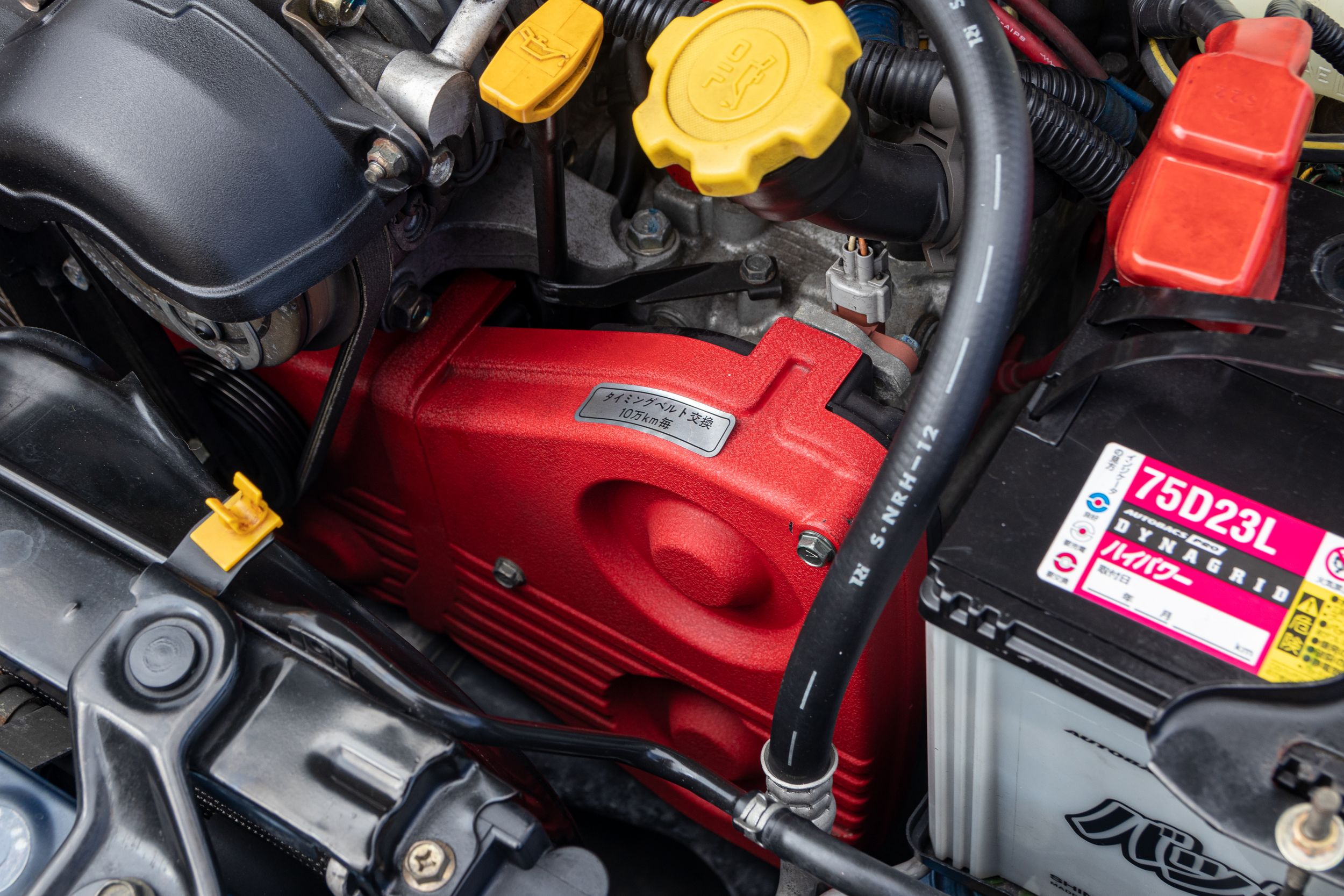 Close-up of red engine bay components with yellow fluid caps.