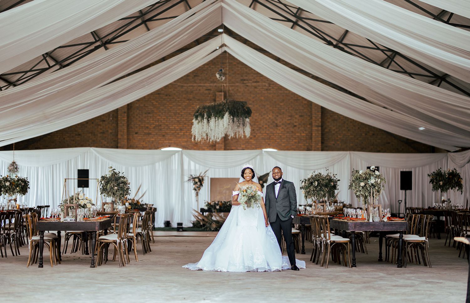 Wedding reception venue with elegant white draping and wooden tables.