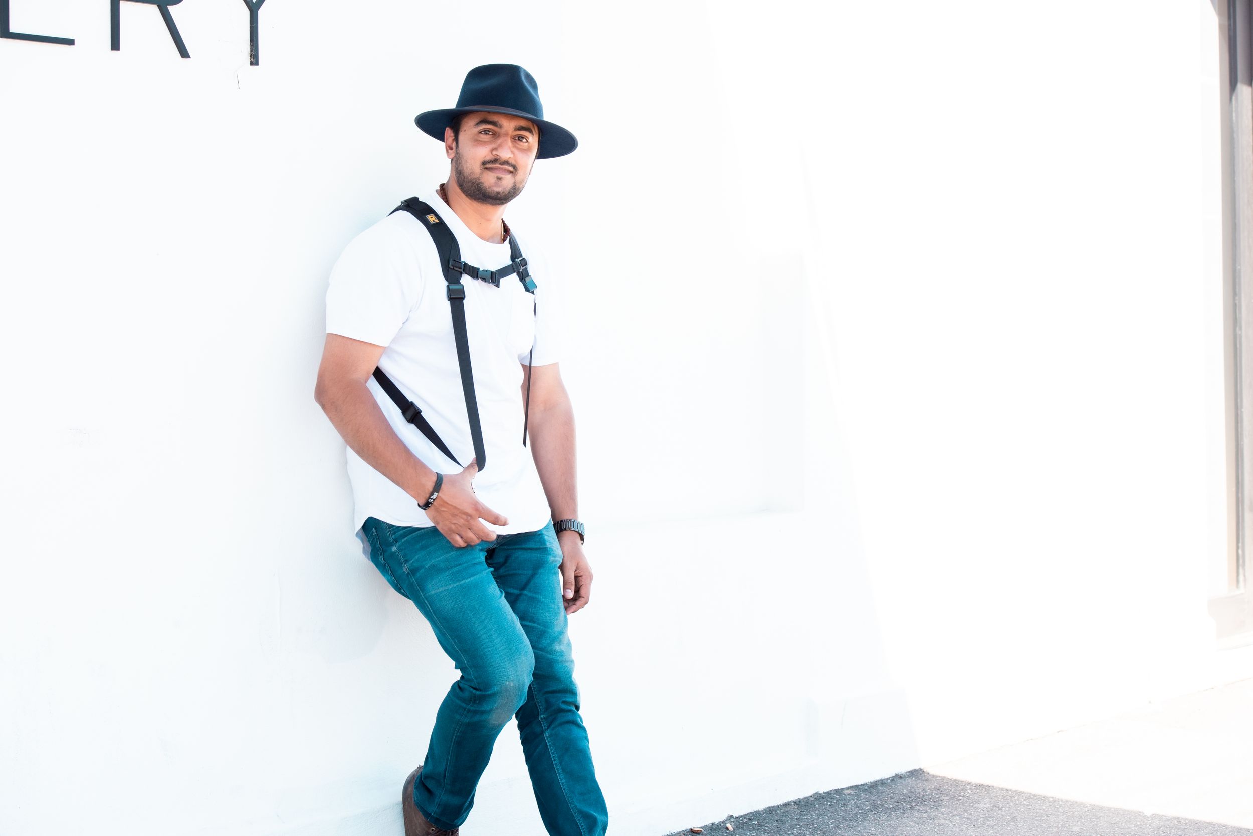Casual portrait of person in fedora and suspenders against white wall.