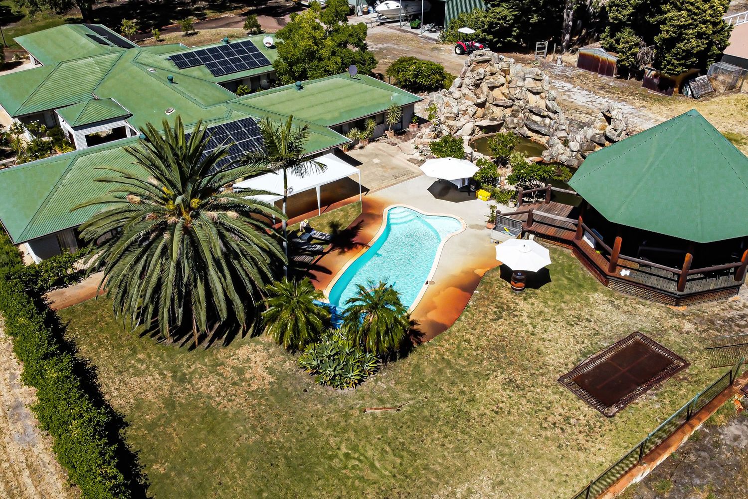 Aerial view of resort venue with swimming pool, palm trees and green shade structures.