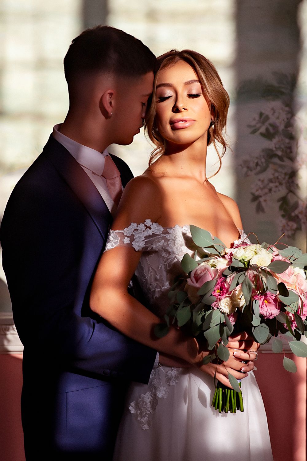 Romantic wedding portrait with bride holding pink bouquet and groom in navy suit.
