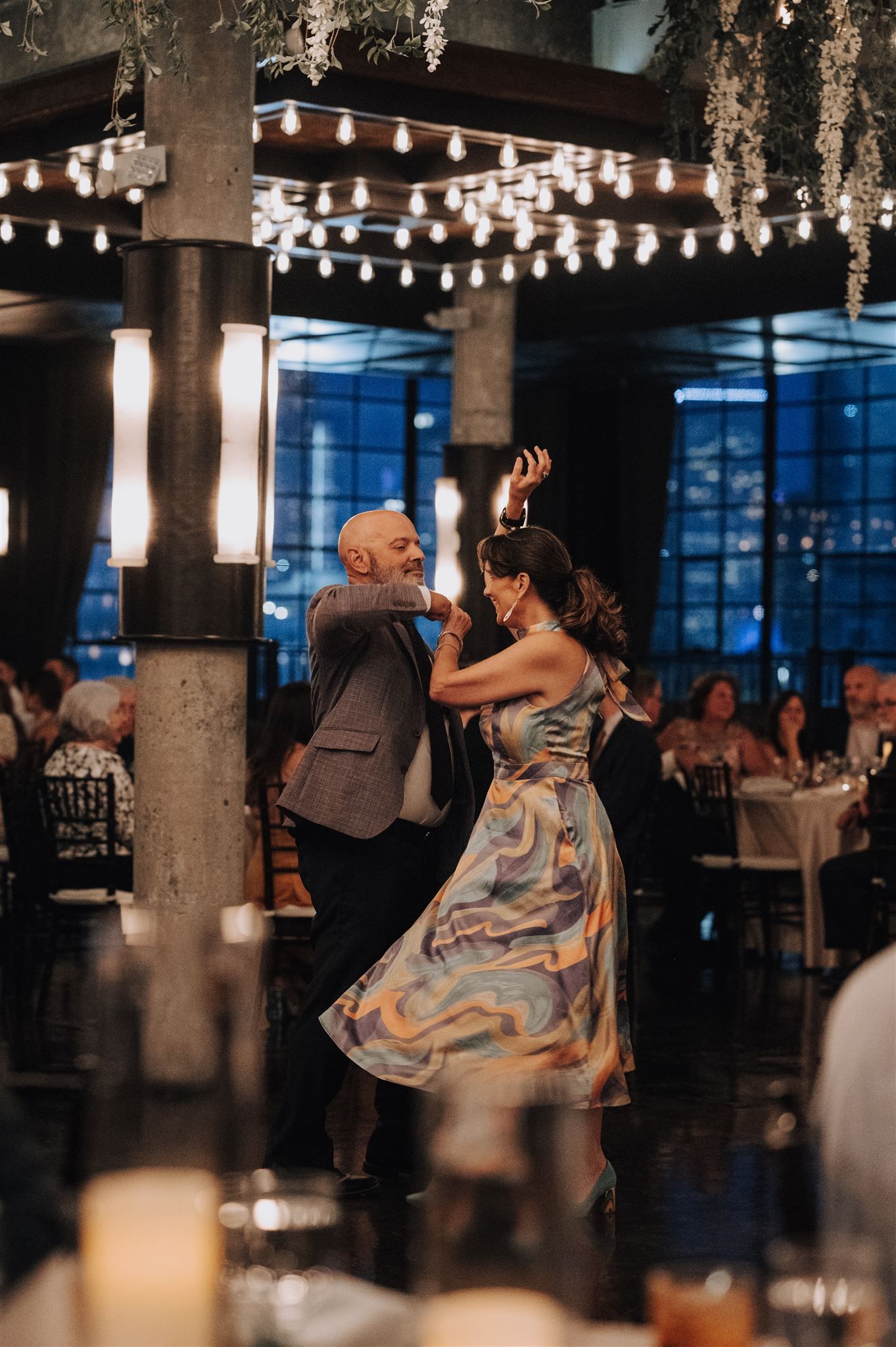 Couple dancing under string lights in an industrial-style wedding venue with exposed columns.