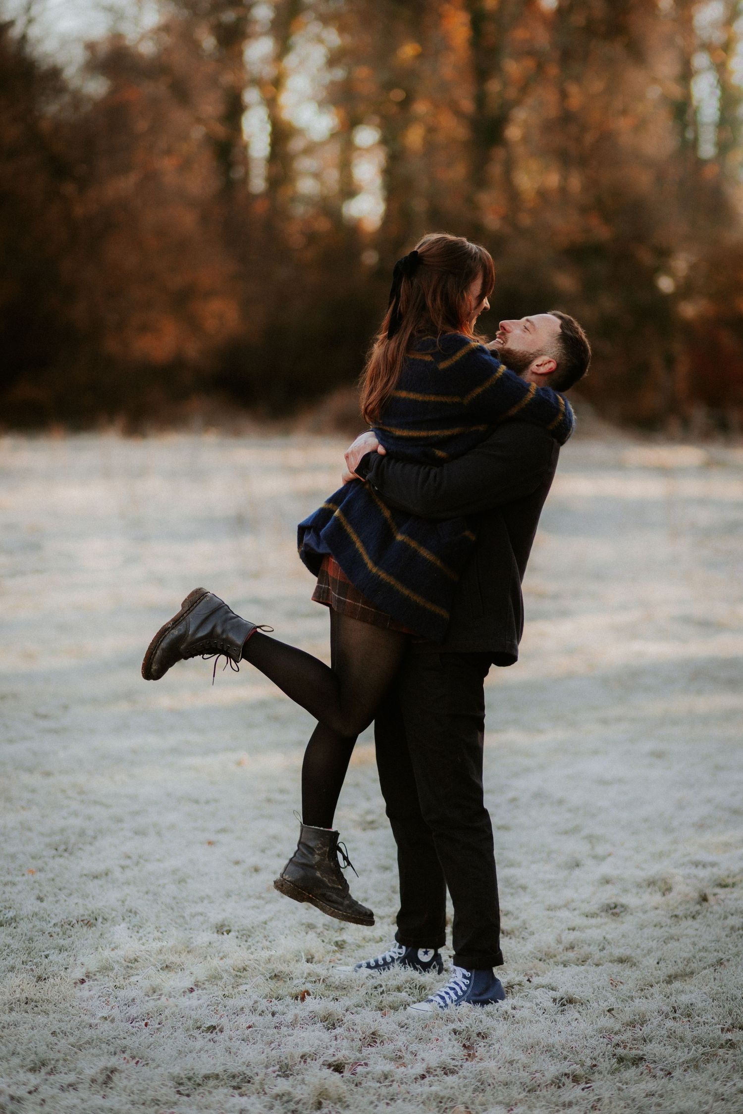 Romantic couple embraces in a frosty winter forest scene with warm autumn colors in the background.