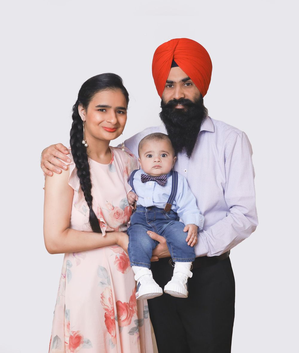Family portrait with man in traditional Sikh turban and woman in floral dress with baby in suspenders.