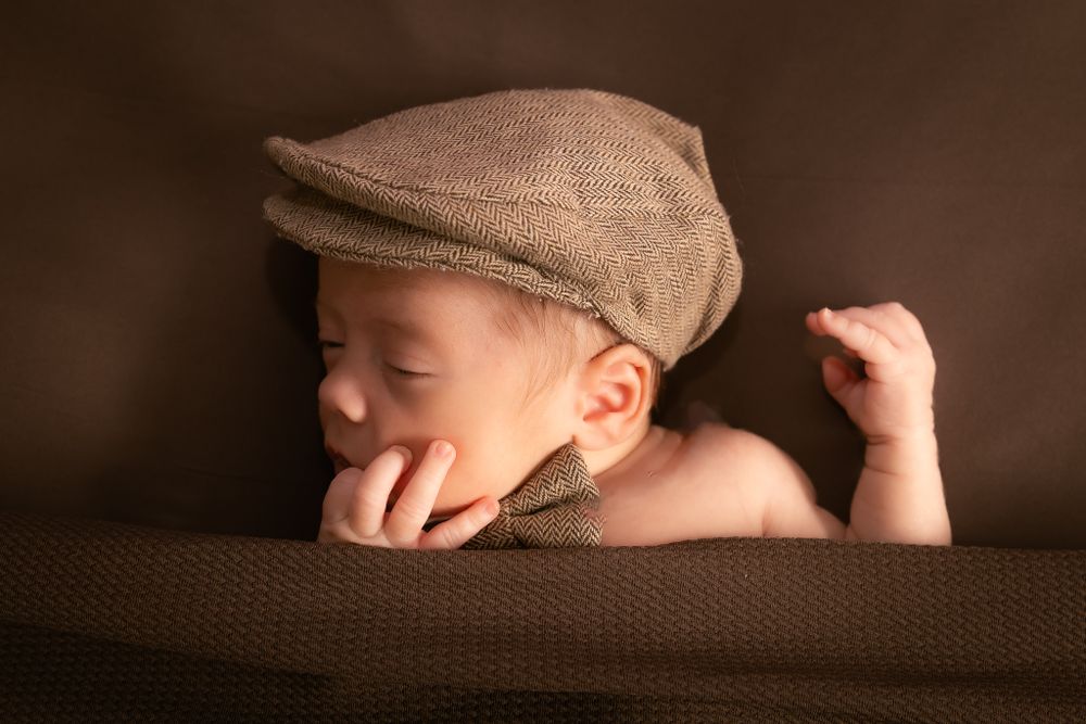 sleeping baby with hat and bowtie in brown blankets