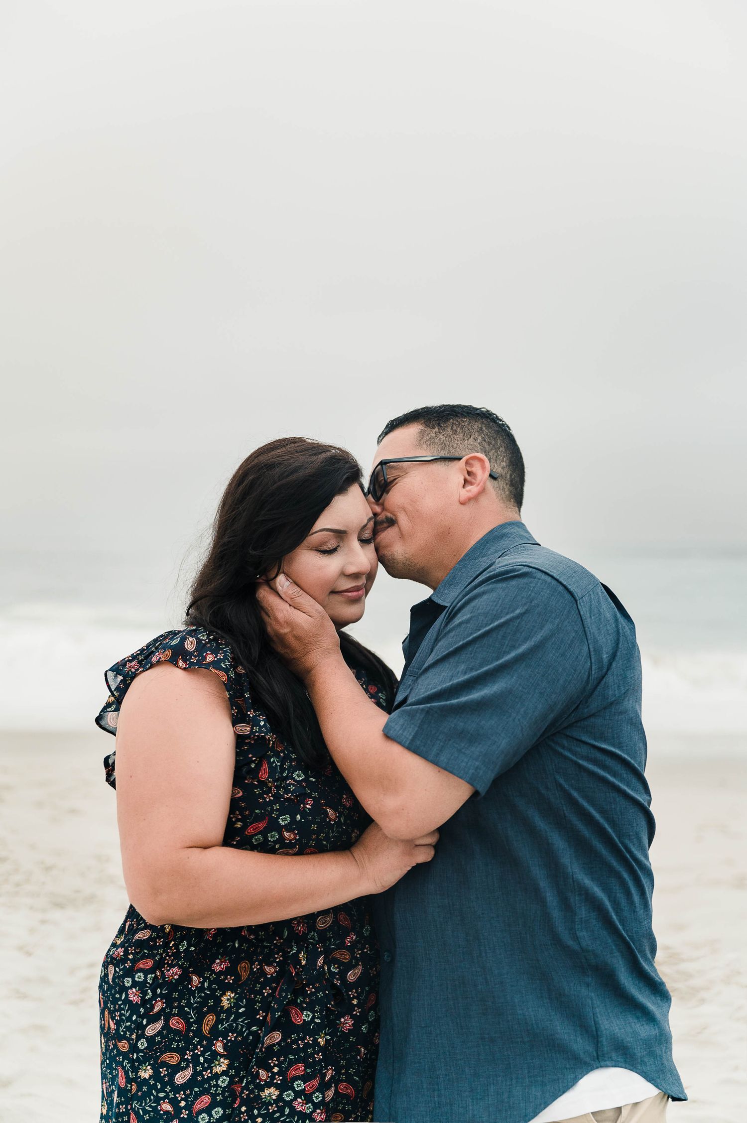 A couple shares an intimate moment on a misty beach.