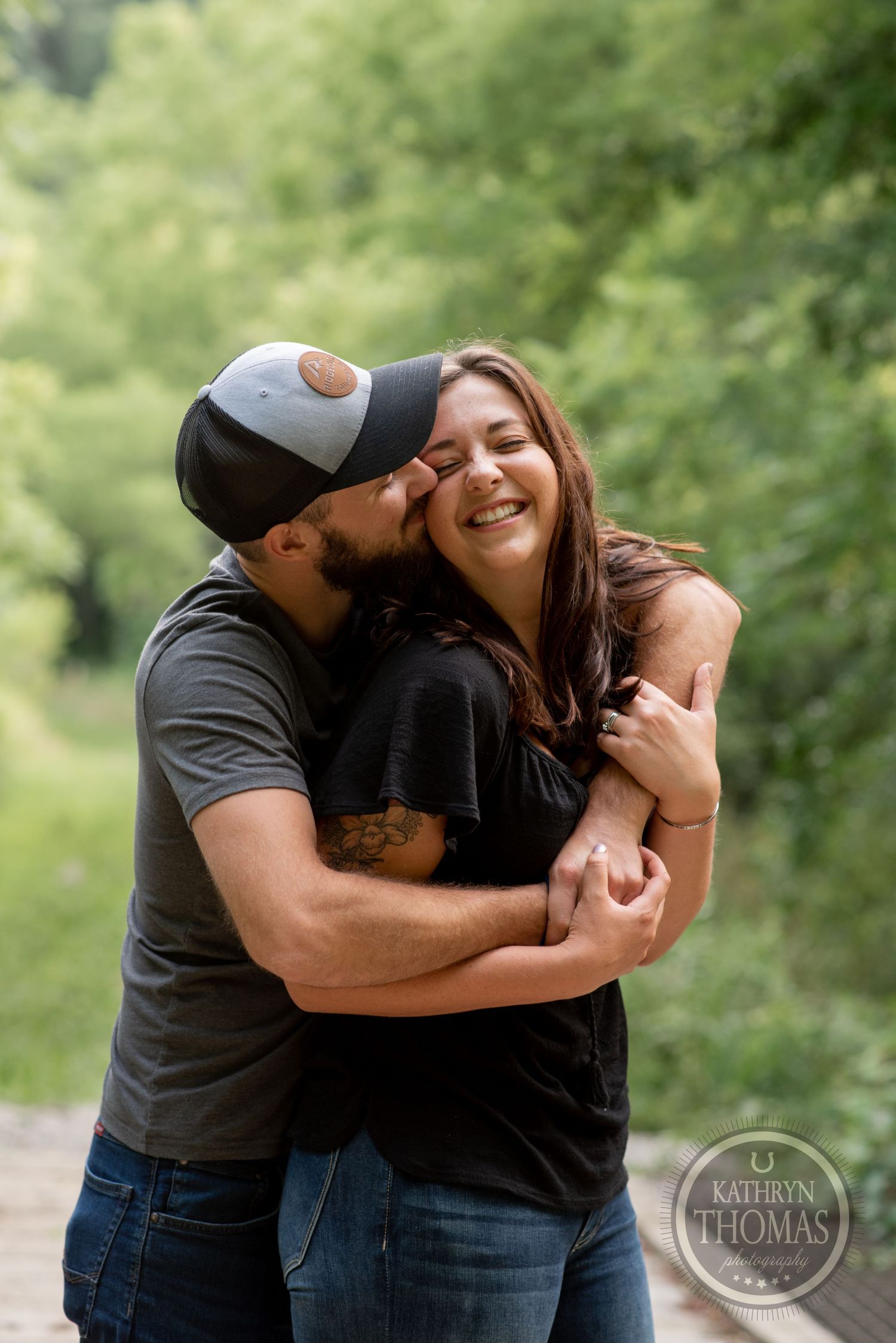 A couple shares a loving embrace while laughing in a sunlit forest.