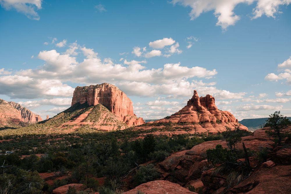 Panoramic view of red rock formations and mountains under a blue sky with white clouds.