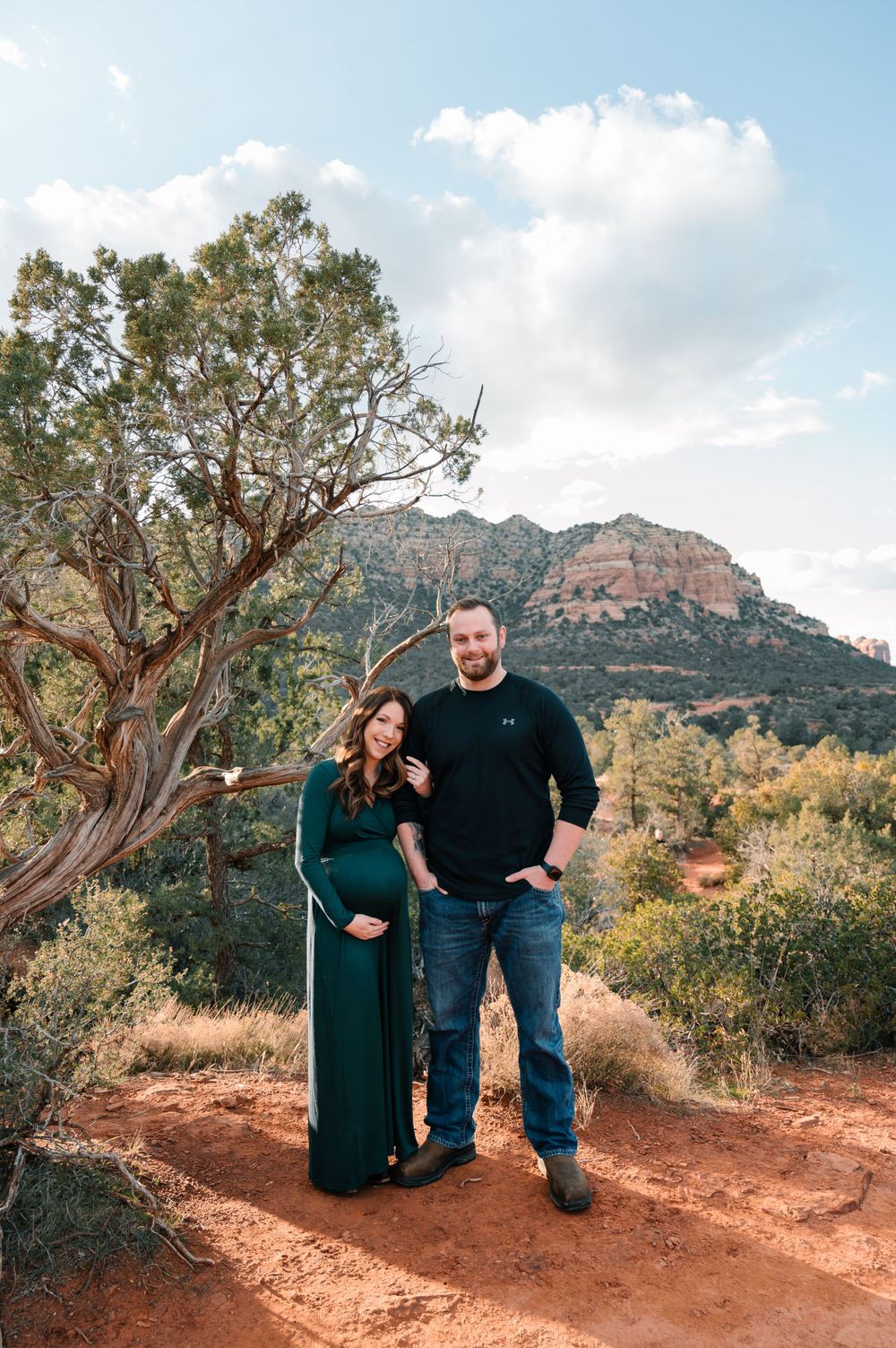 A couple poses together on red rocks with mountain views in the background.