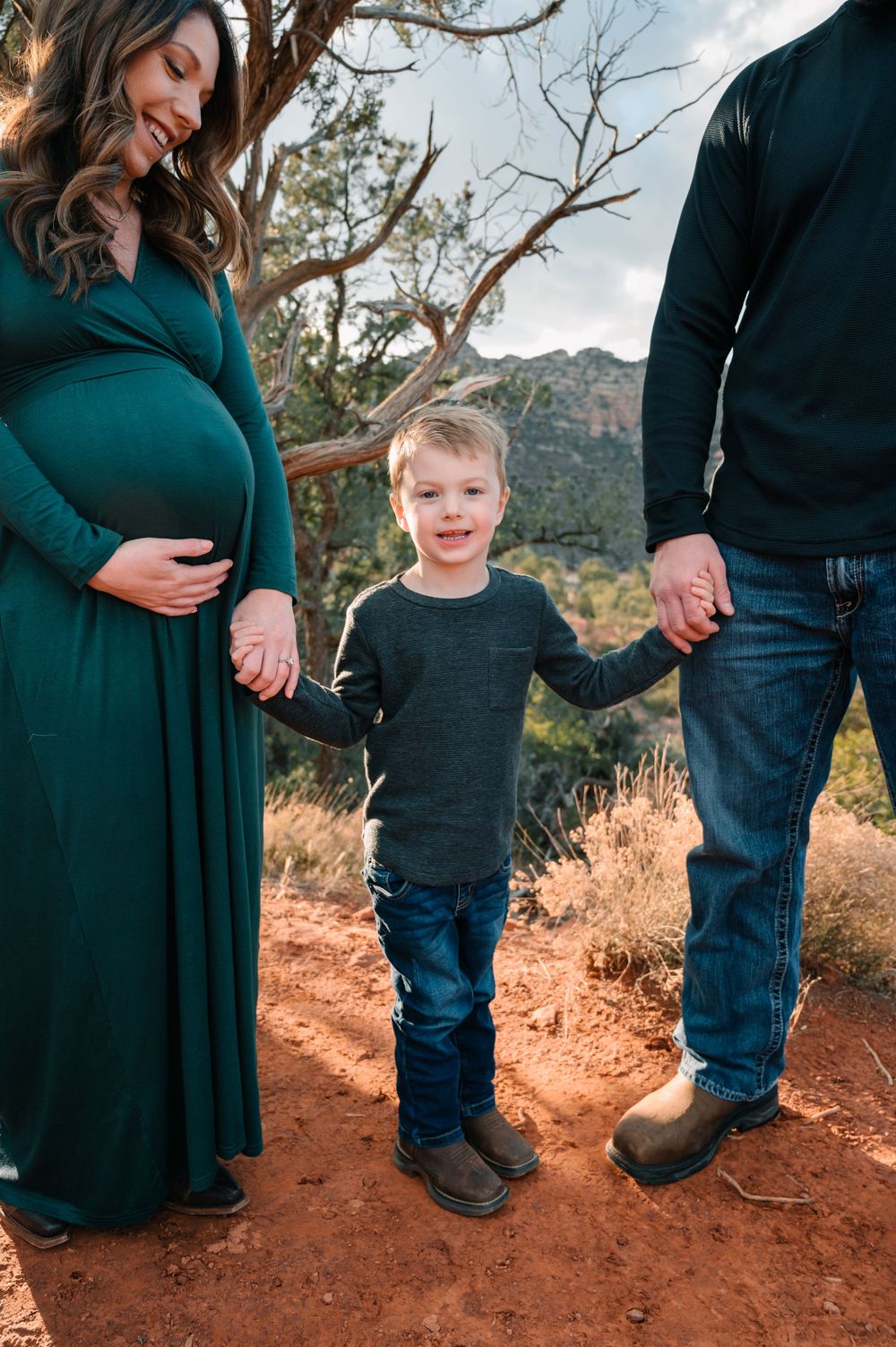 Family members hold hands while standing on red desert soil with mountains in the background.