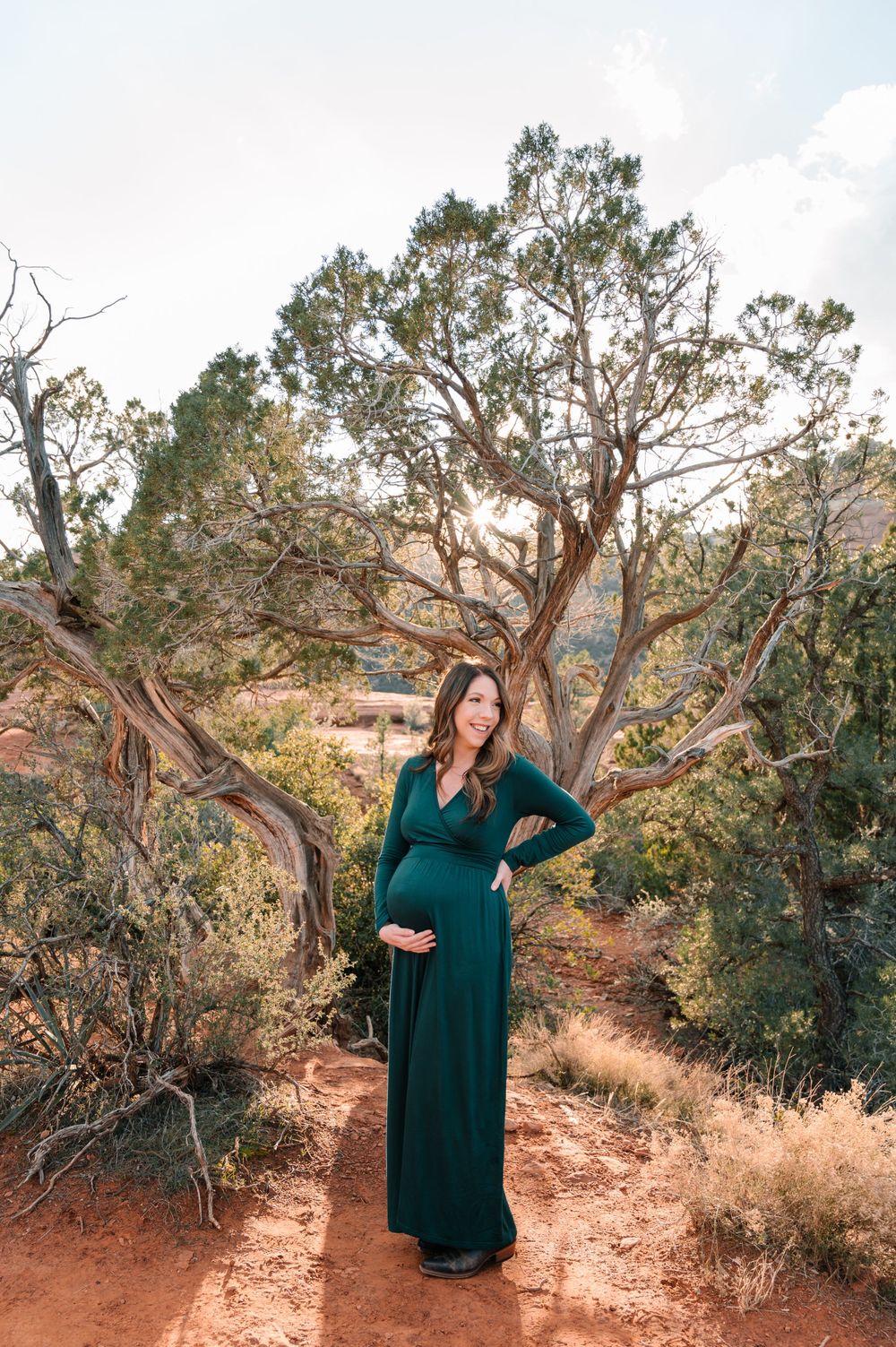 Maternity photoshoot in a rustic desert setting with red rocks and gnarled trees.