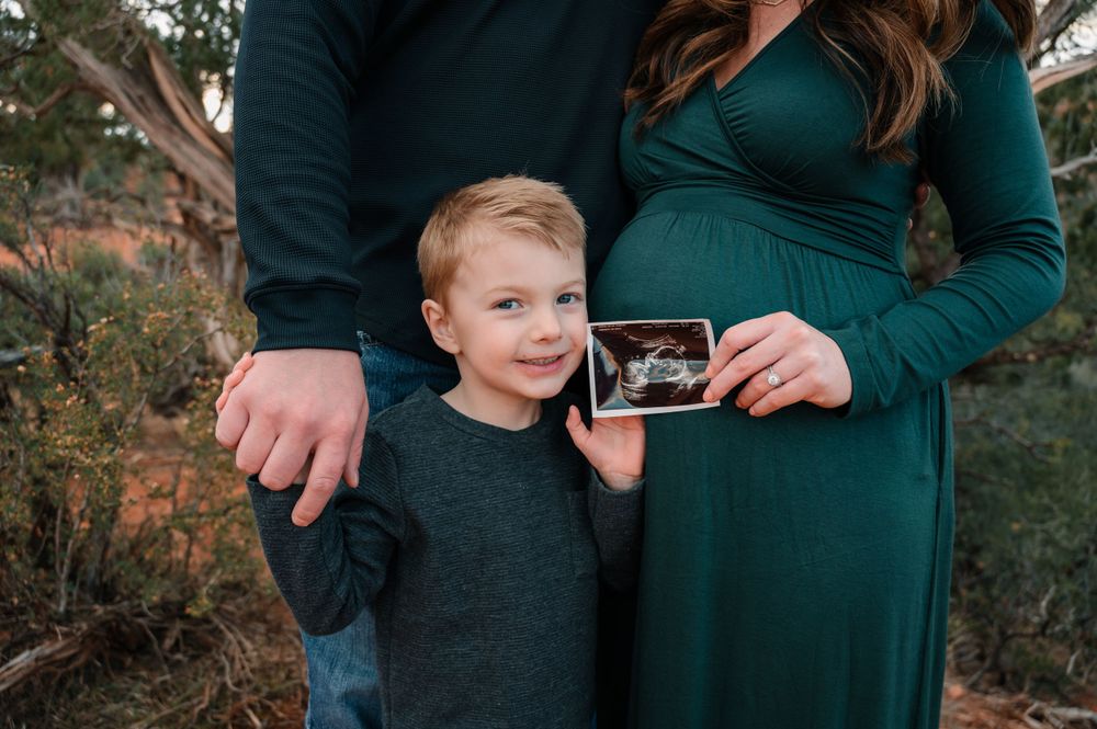 Family members hold up ultrasound photo during outdoor desert photo session.