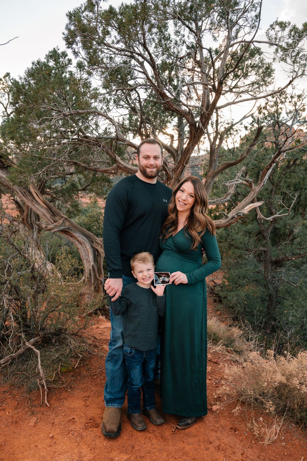 Family portrait session captured against rugged desert landscape with twisted trees.