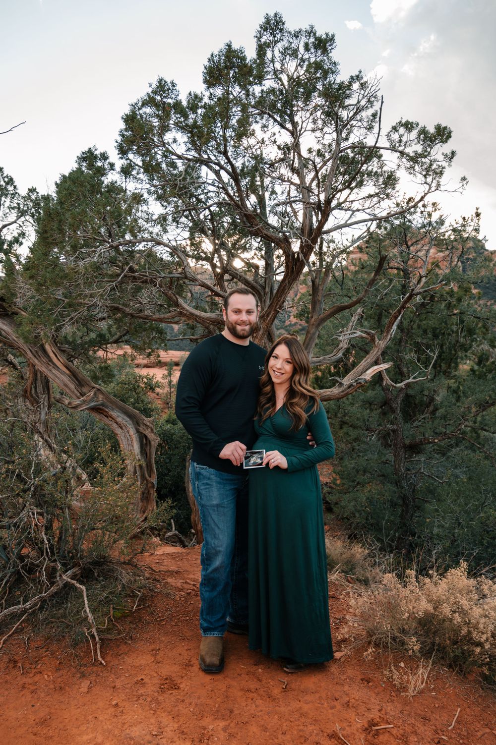 Couple shares intimate moment while holding ultrasound photo in desert setting.