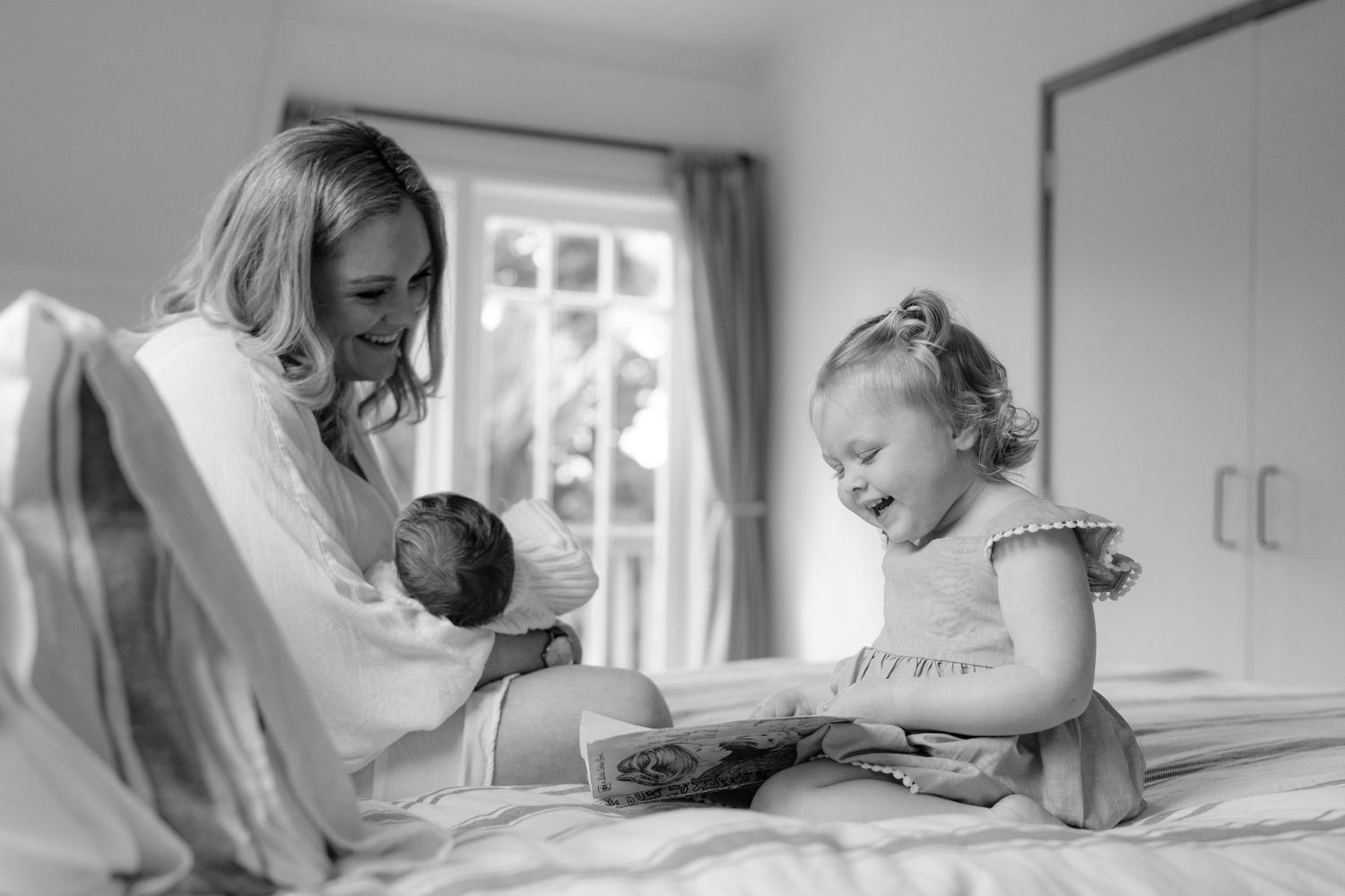 Toddler reading book with Mum and Baby.  Candid Family portraits Auckland