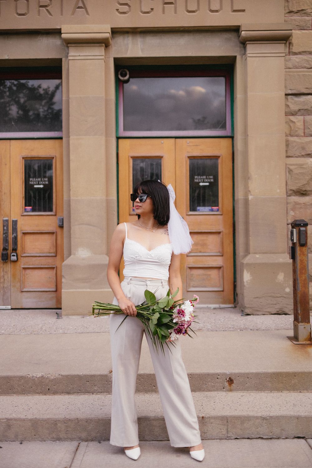 Elegant poses with flowers in front of a historic school building entrance.