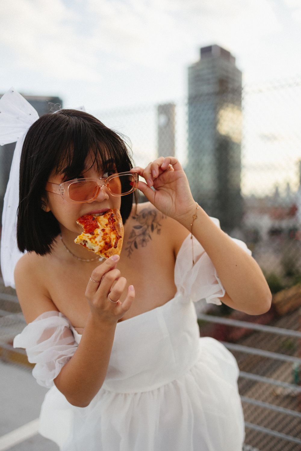 Playful moments enjoying pizza on a rooftop with city buildings in the background.