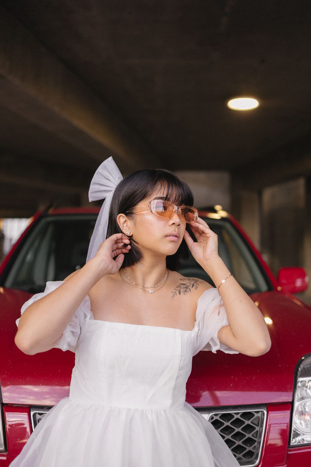 Stylish poses in a dimly lit parking garage with a red car in the background.
