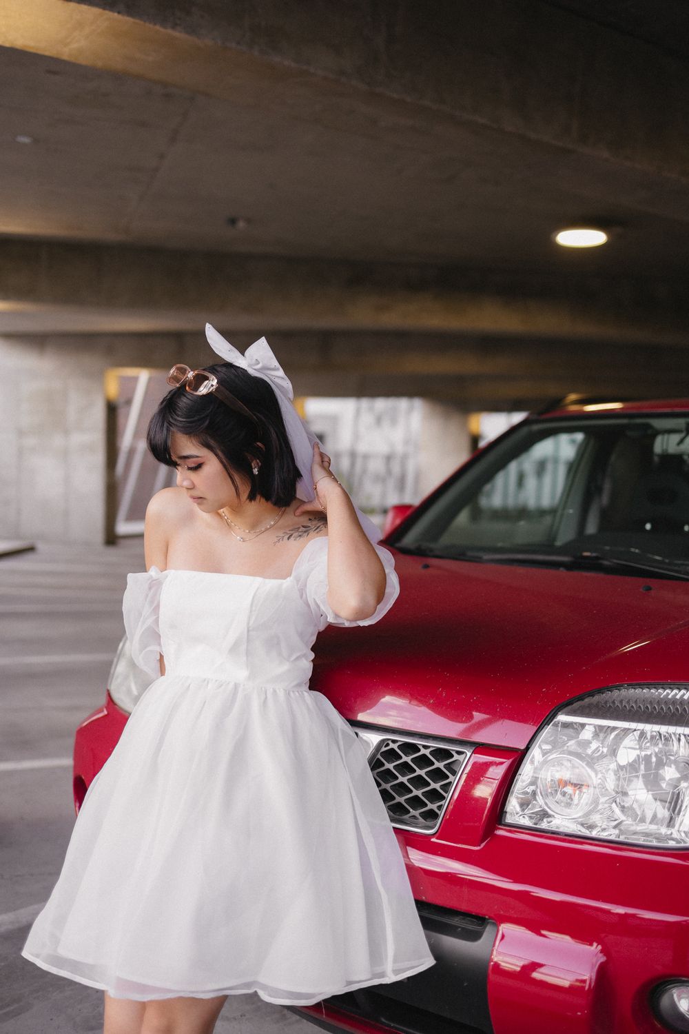 Artistic shots in a parking garage featuring a red car and white dress ensemble.