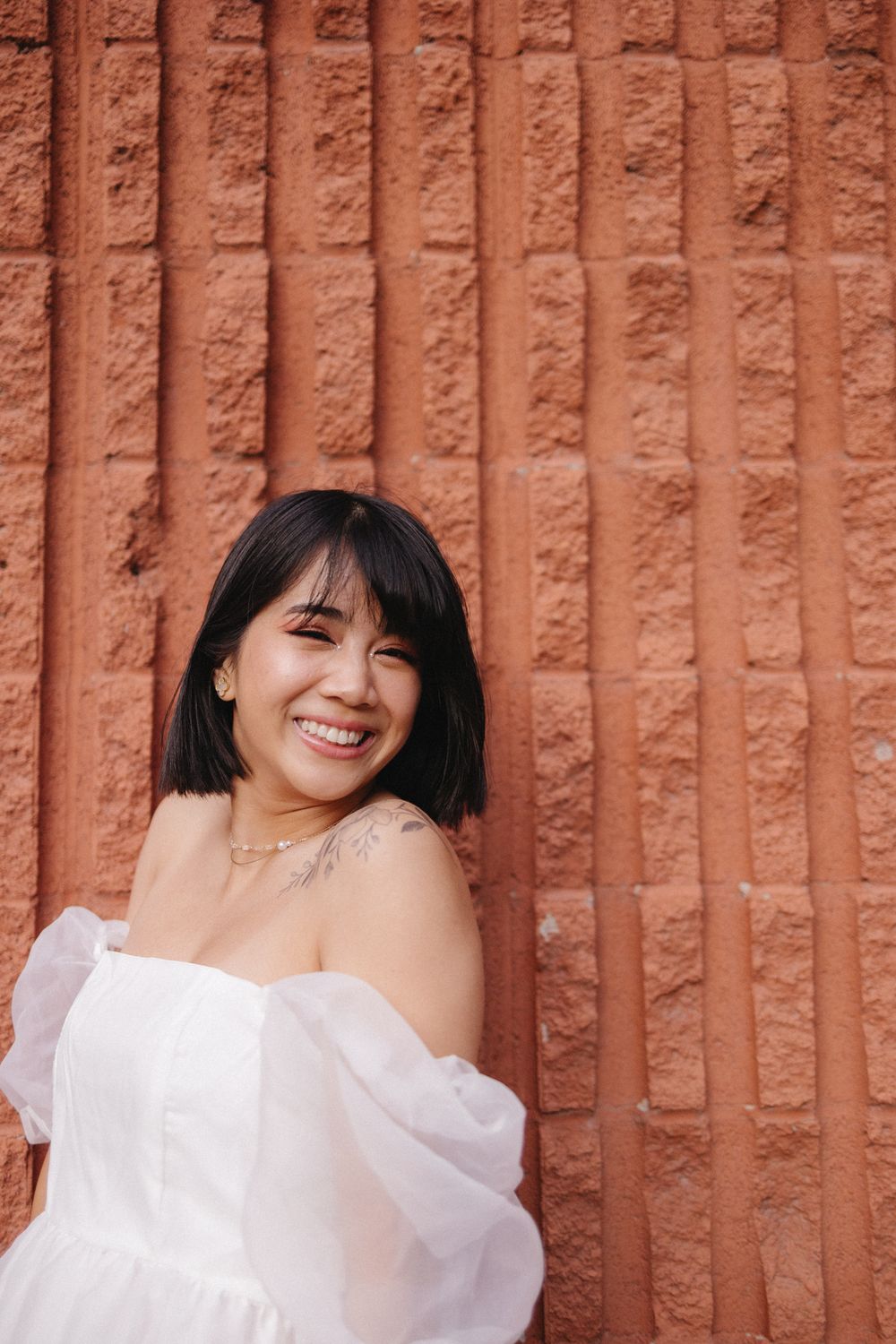 Candid portrait session showcasing bright smiles and white clothing against a textured brick background.