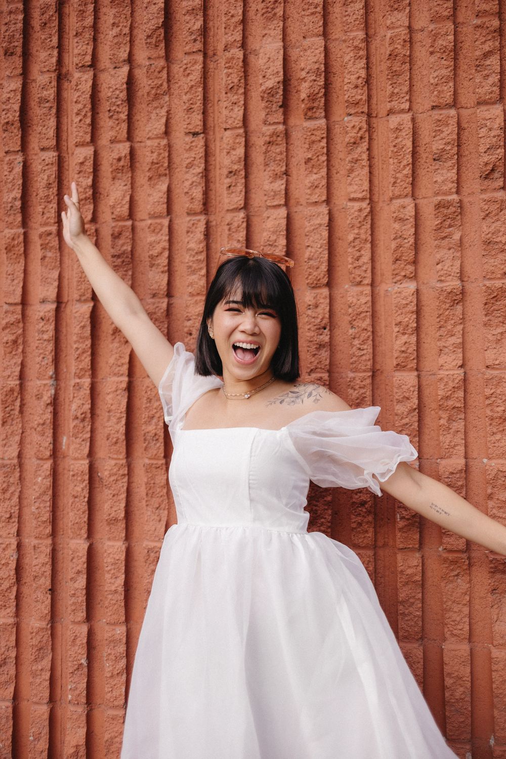 A joyful photoshoot against a terracotta wall featuring flowing white outfits and expressive poses.