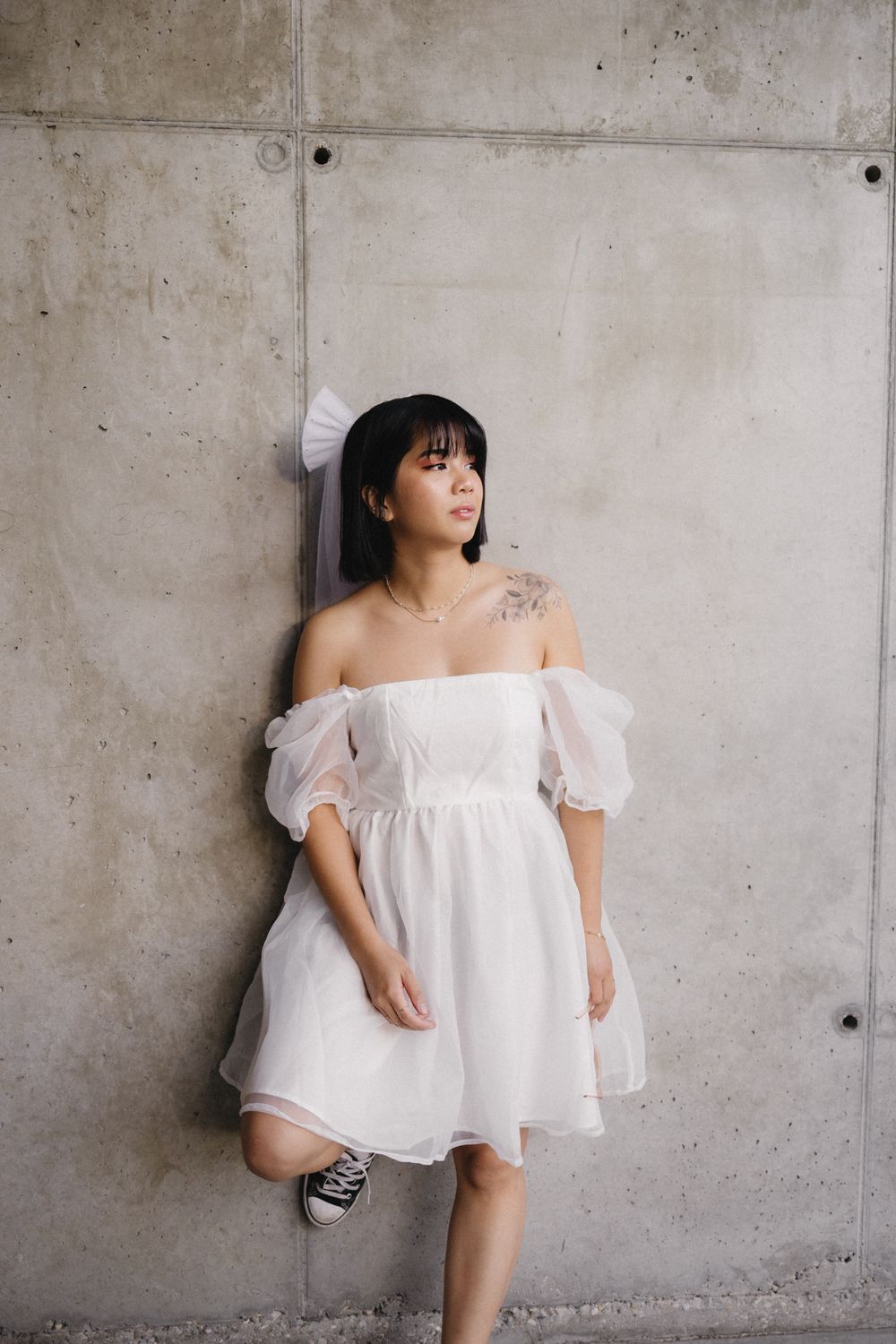 Playful poses against a concrete wall wearing an ethereal white off-shoulder dress.