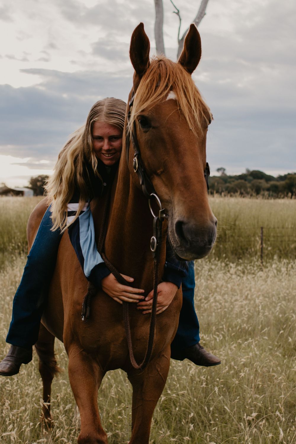 girl sitting on horse, giving horse a hug in a paddock