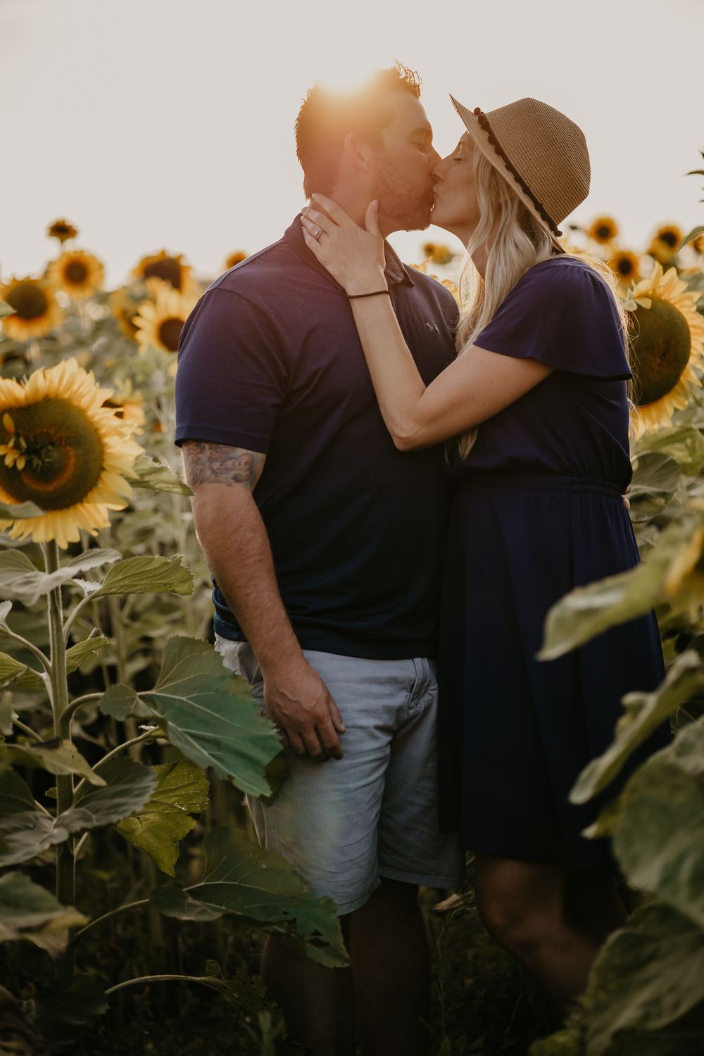 Romantic couple embracing in a sunflower field during golden hour sunset.