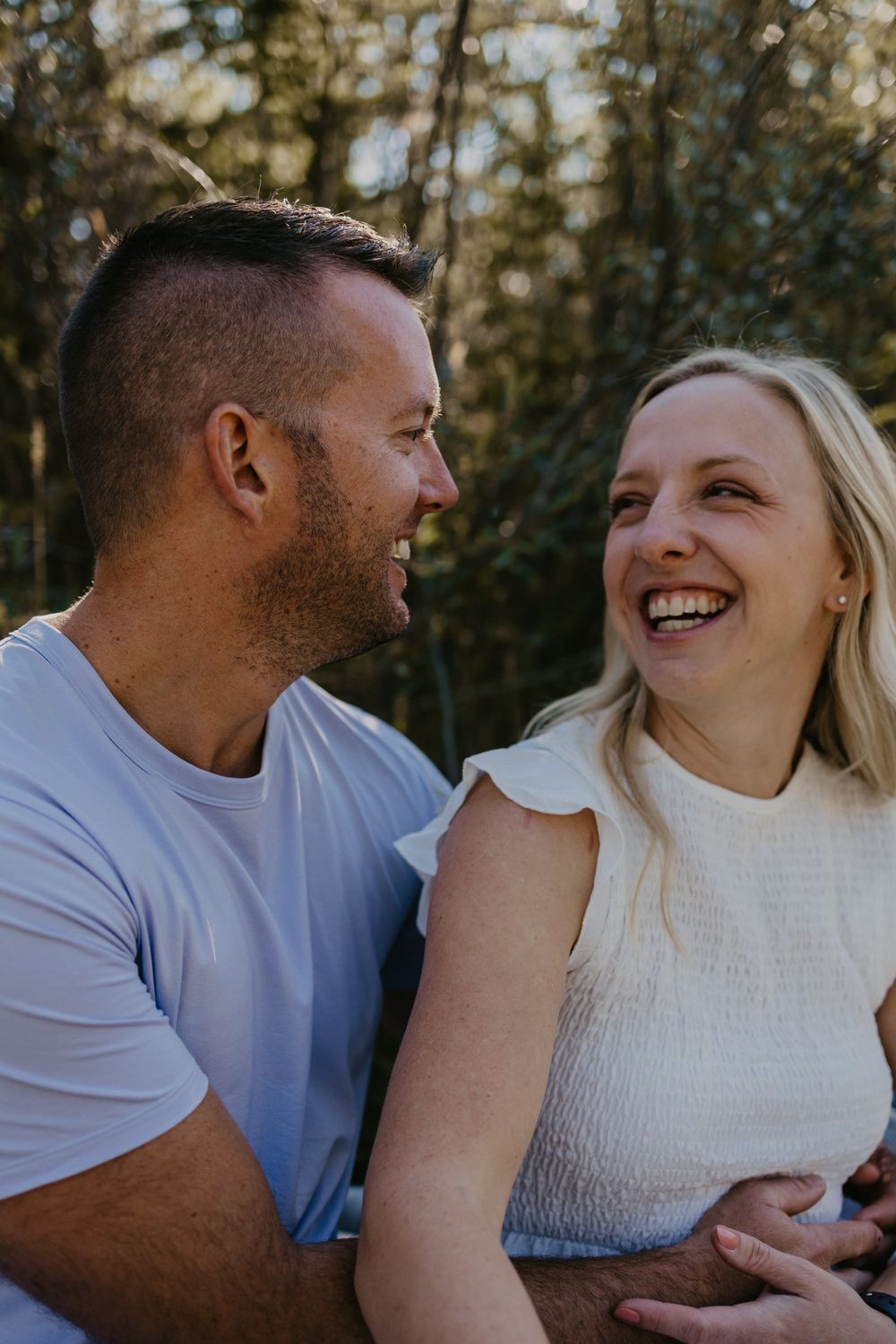 Candid outdoor portrait of a laughing couple sharing a joyful moment in natural lighting.