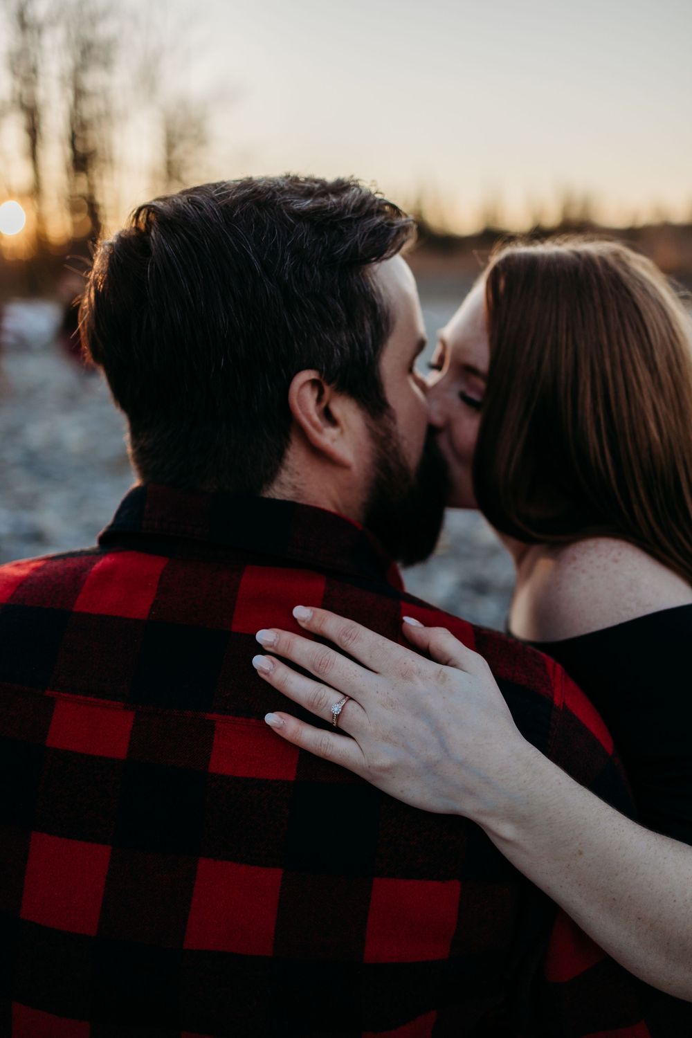 A romantic couple shares a tender moment wearing plaid flannel against a sunset backdrop.