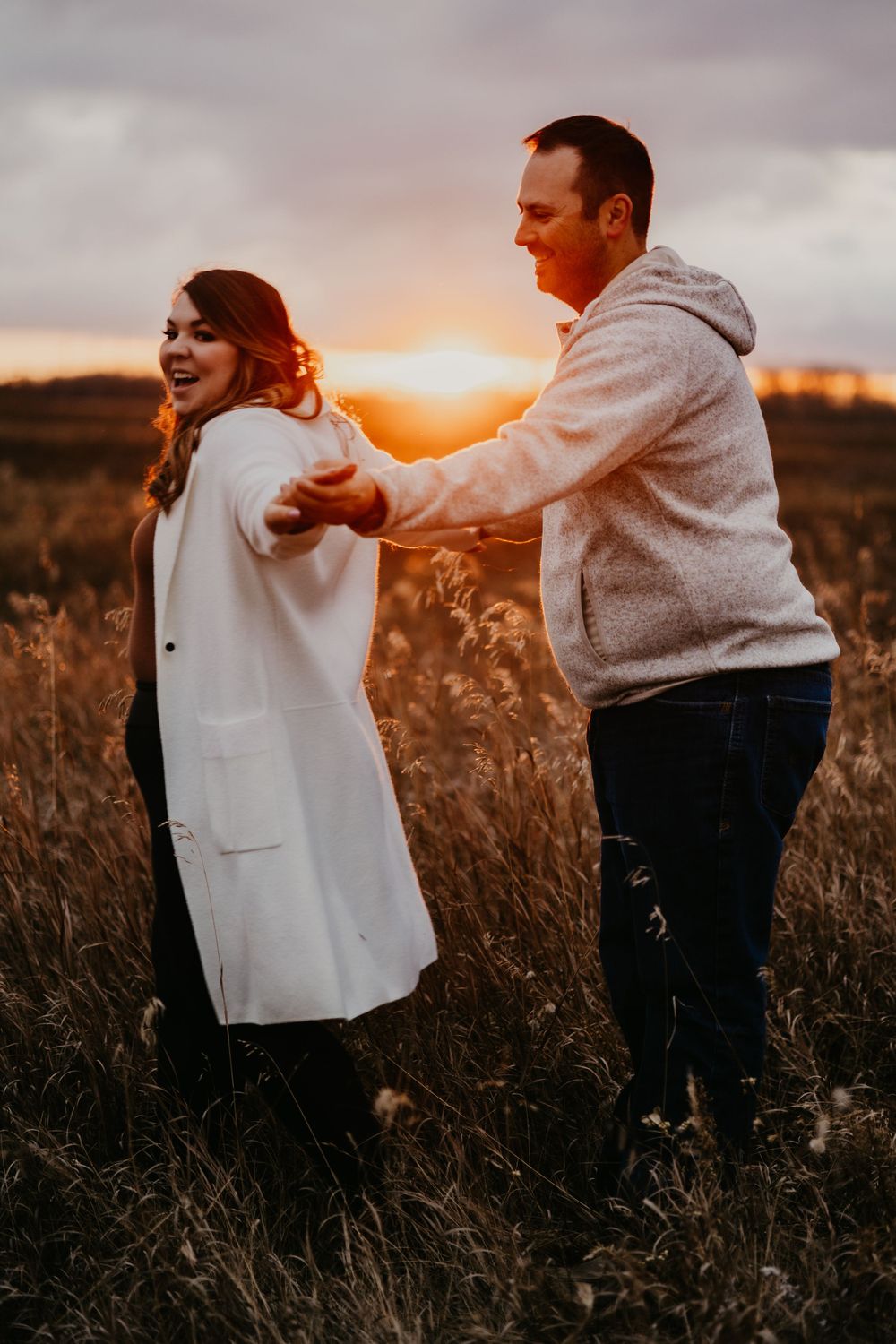 A couple dances and laughs together in a field during a golden sunset.