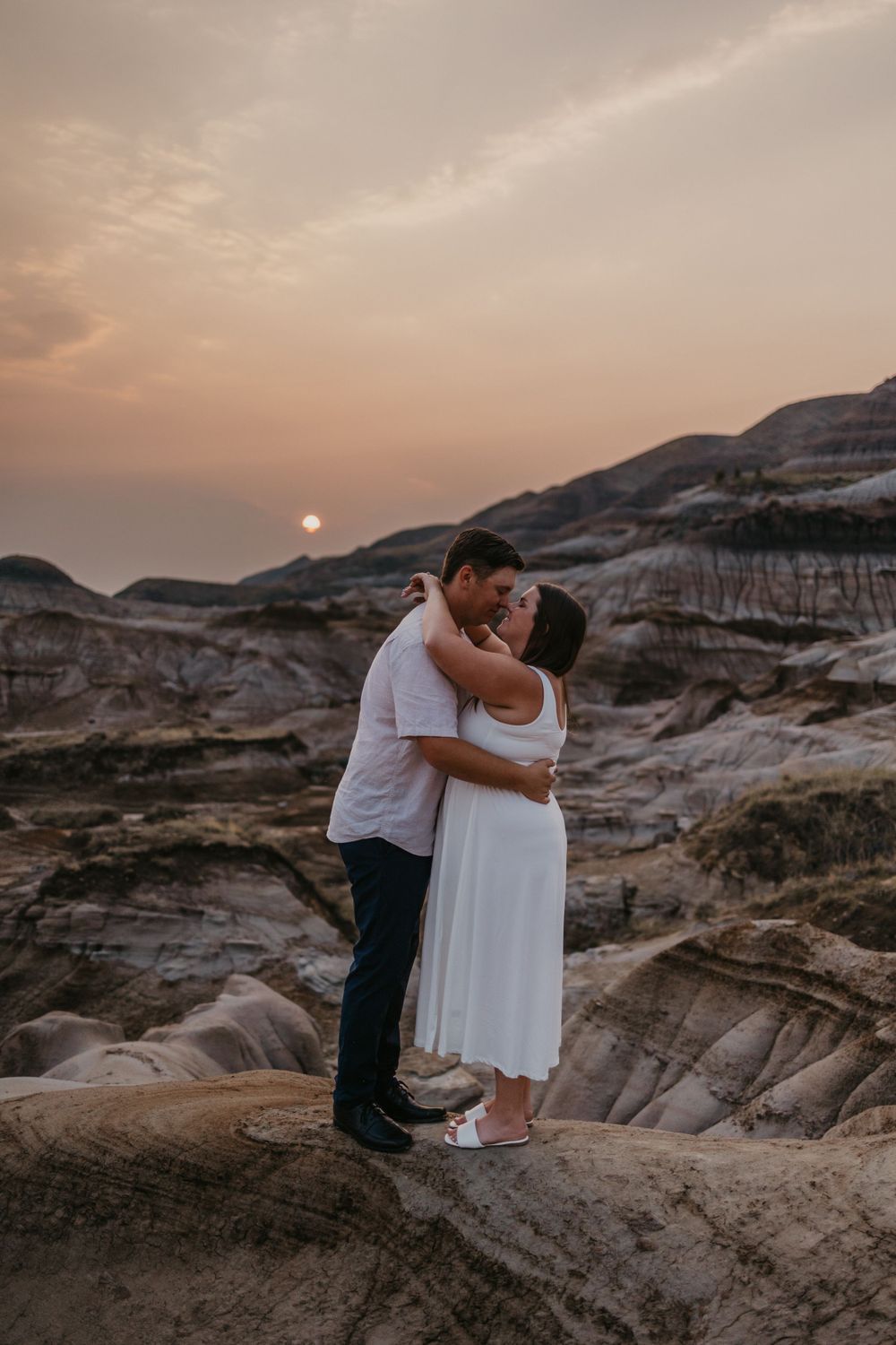 Romantic couple embraces against stunning desert badlands landscape at sunset.