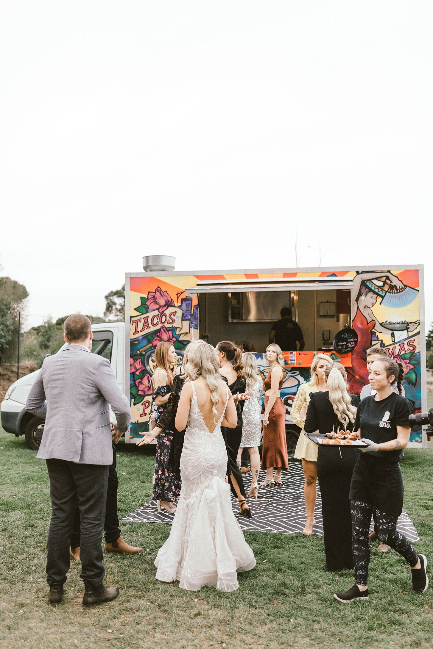 Wedding celebration with guests gathering around colorful food truck on lawn.