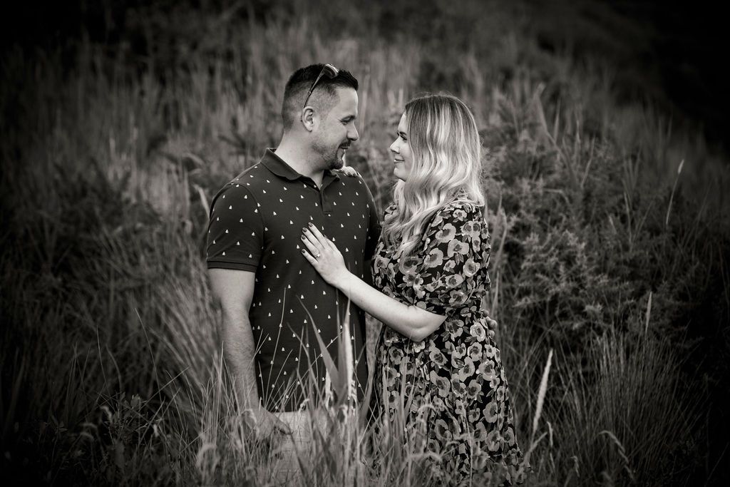 A romantic black and white portrait of a couple standing in tall grass.