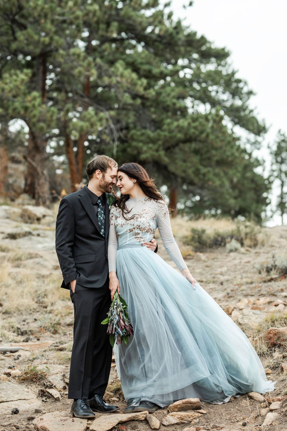 A couple in formal attire shares an intimate moment against a rocky mountain landscape.