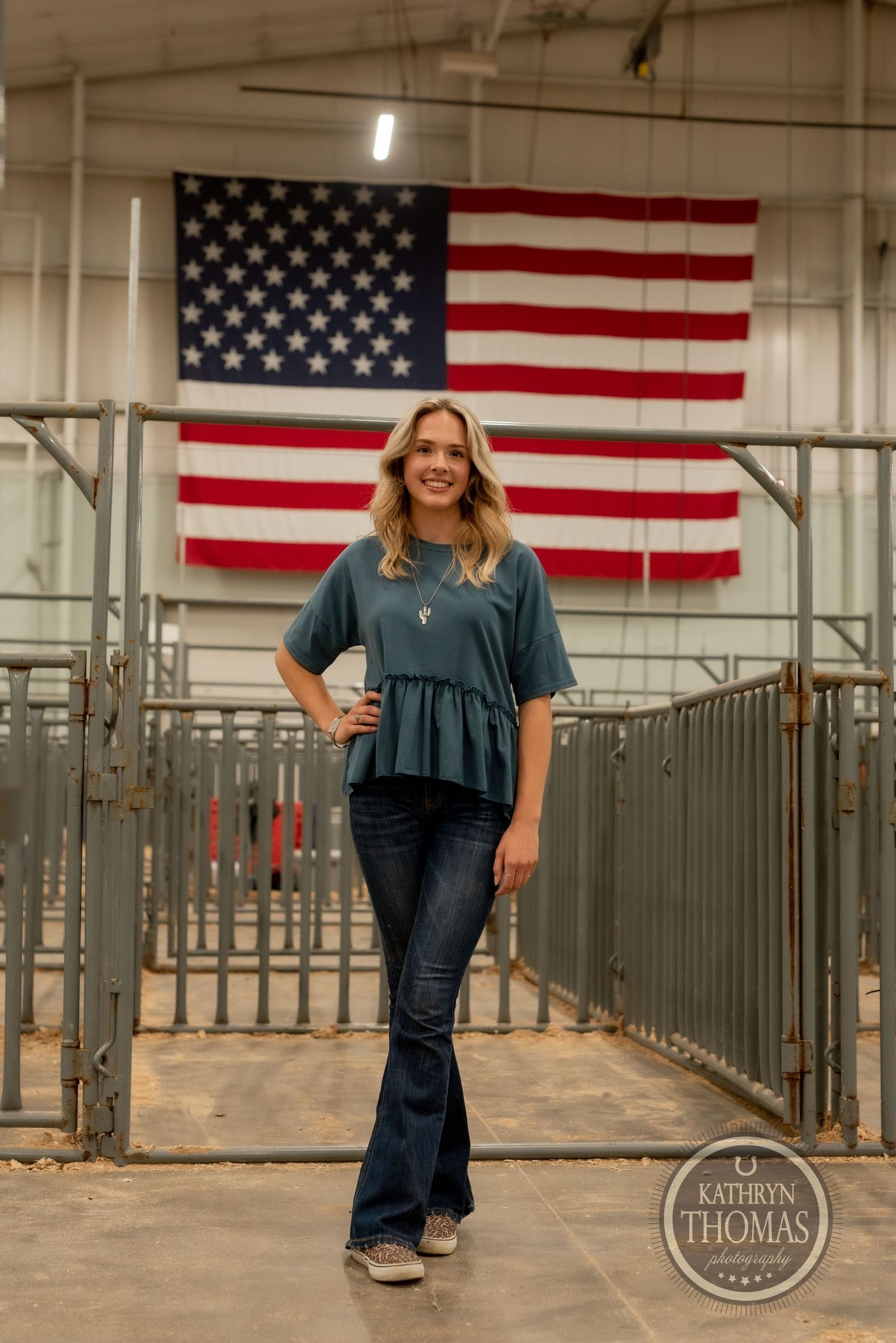 Full-length fashion portrait against American flag showing teal peplum top and flared denim.