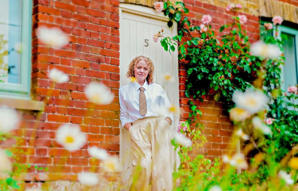 A vintage-style portrait showing a person standing by a brick wall with blooming flowers.