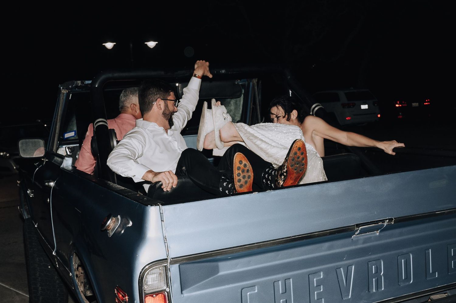 Wedding party celebrating in the back of a classic Chevrolet pickup truck at night.