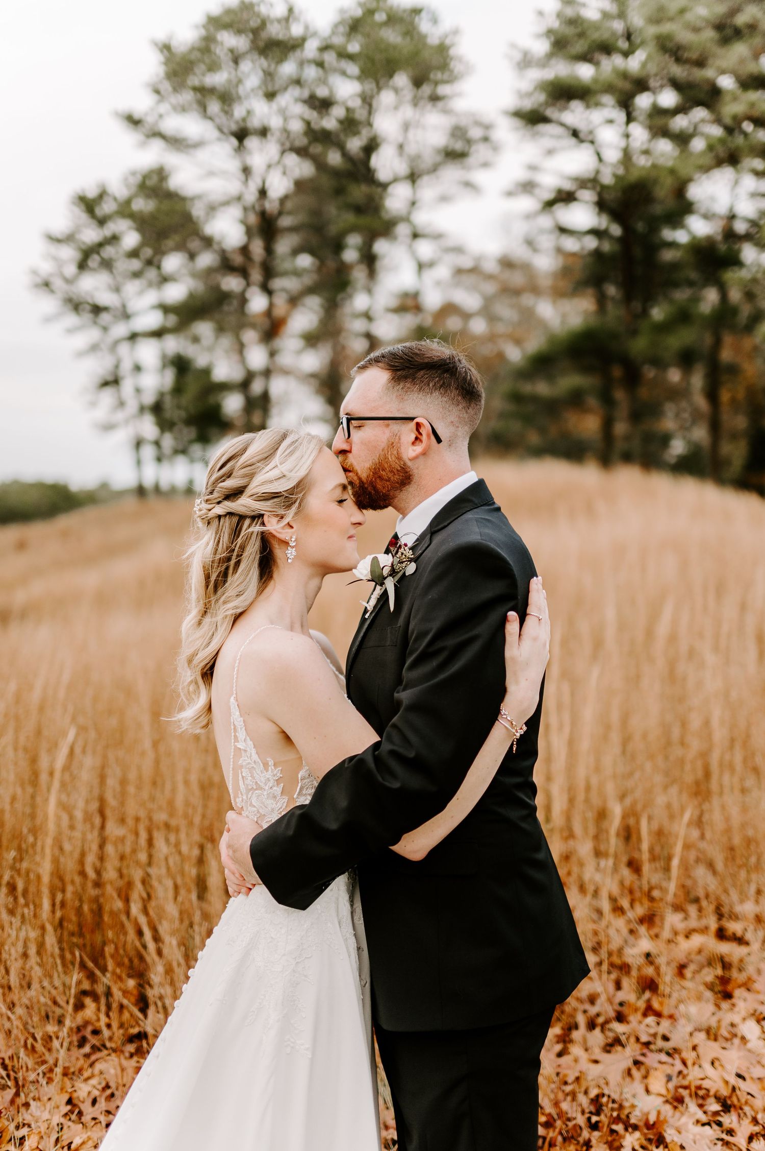 Emotional wedding moment photographed against a backdrop of autumn foliage and pine trees.