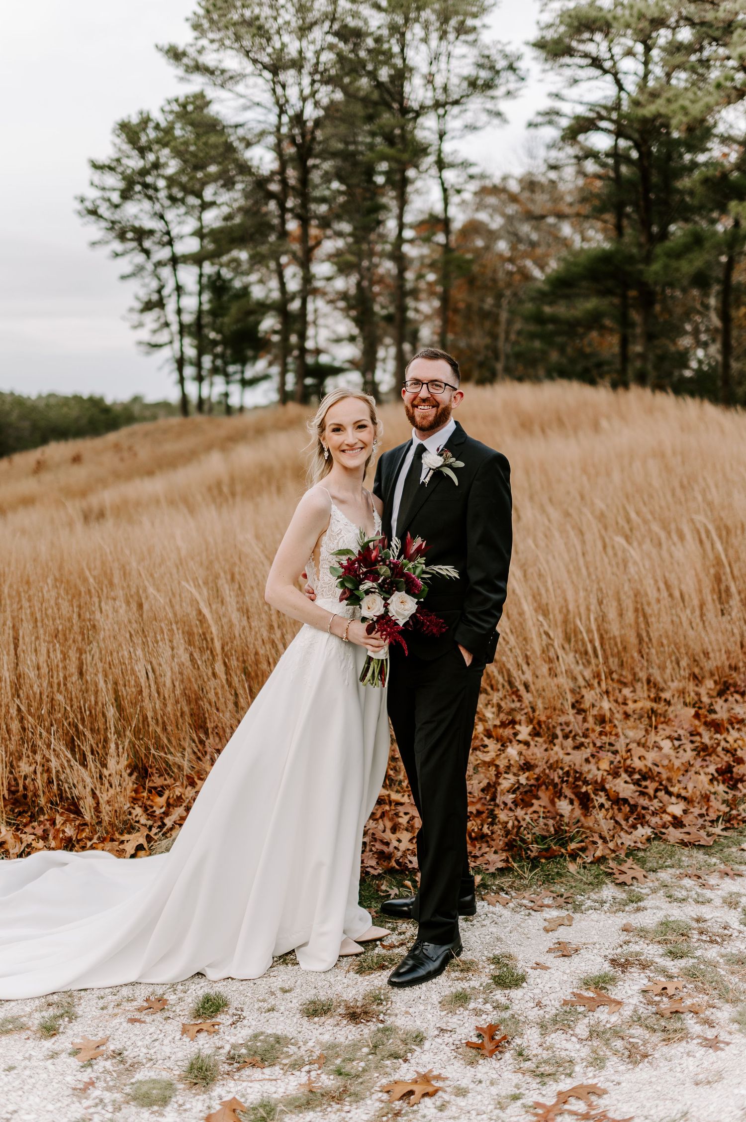A romantic wedding photoshoot in a field of golden autumn grass with pine trees in the background.