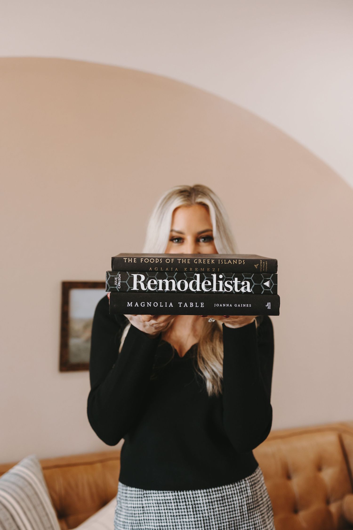 Woman in black sweater holding up Remodelista book against pink wall.