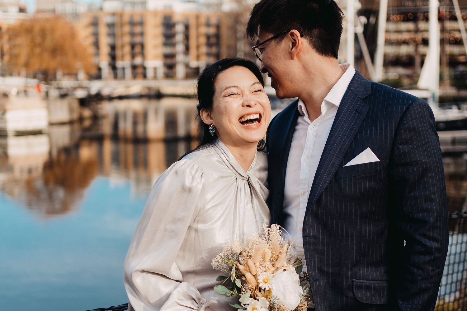 Couple sharing joyful moment near marina with autumn buildings in background.