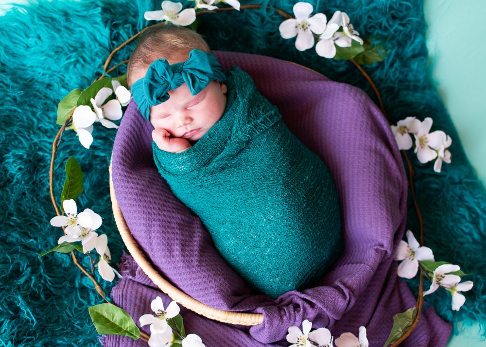 newborn daughter with teal wrap, purple blanket, flowers