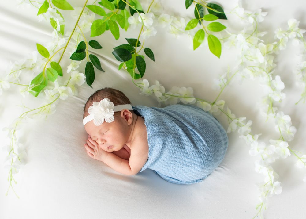 sleeping newborn photo with blue wrap and white flowers with green leaves